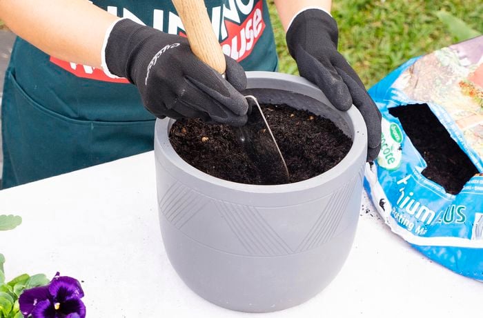 A person making a hole for a plant in a pot of soil