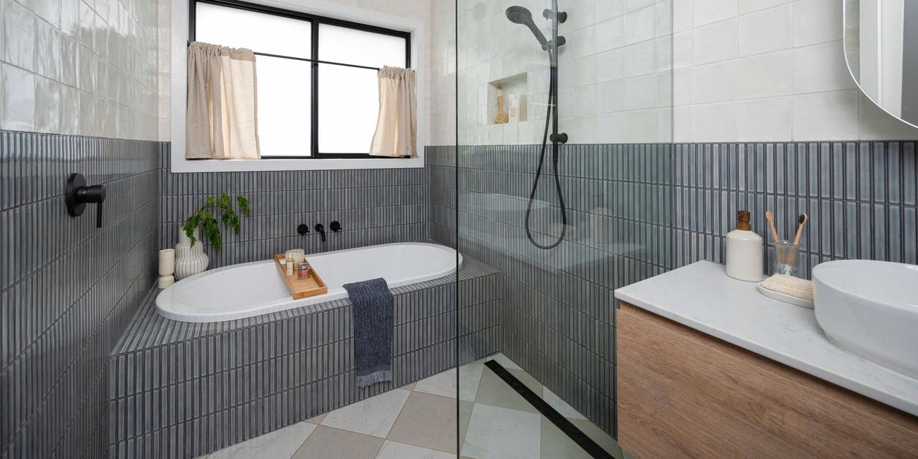 A modern bathroom with grey tiles on the walls, a shower, bath and basin in it