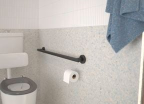 Bathroom with black handrail, white floor and wall tiles and green hand towel hanging on the wall.
