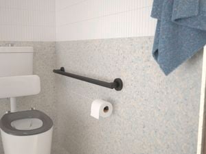 Bathroom with black handrail, white floor and wall tiles and green hand towel hanging on the wall.