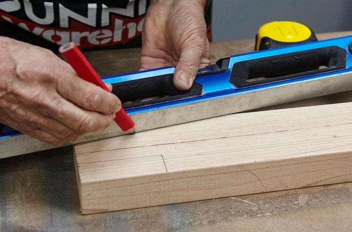 A spirit level and a pencil being used to rule an angled cut marker into a piece of timber