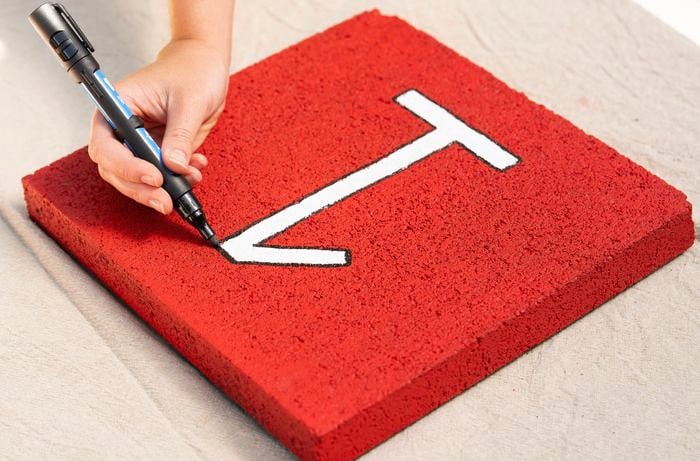 A person is outlining the hopscotch numbers on a red paver tile to create a colourful DIY hopscotch path.
