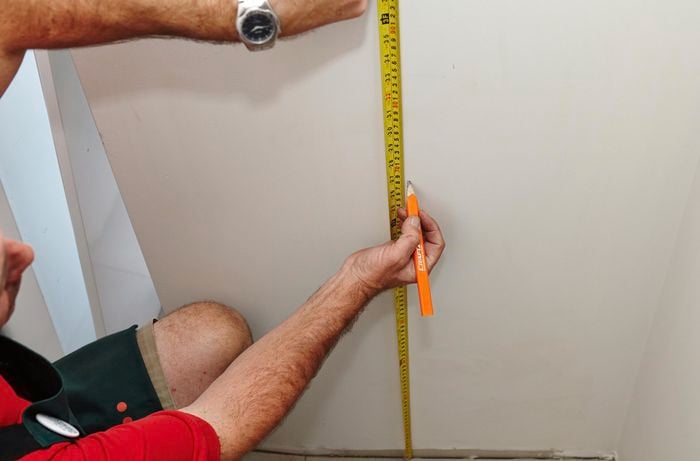 Using a measuring tape and pencil to mark the wall.