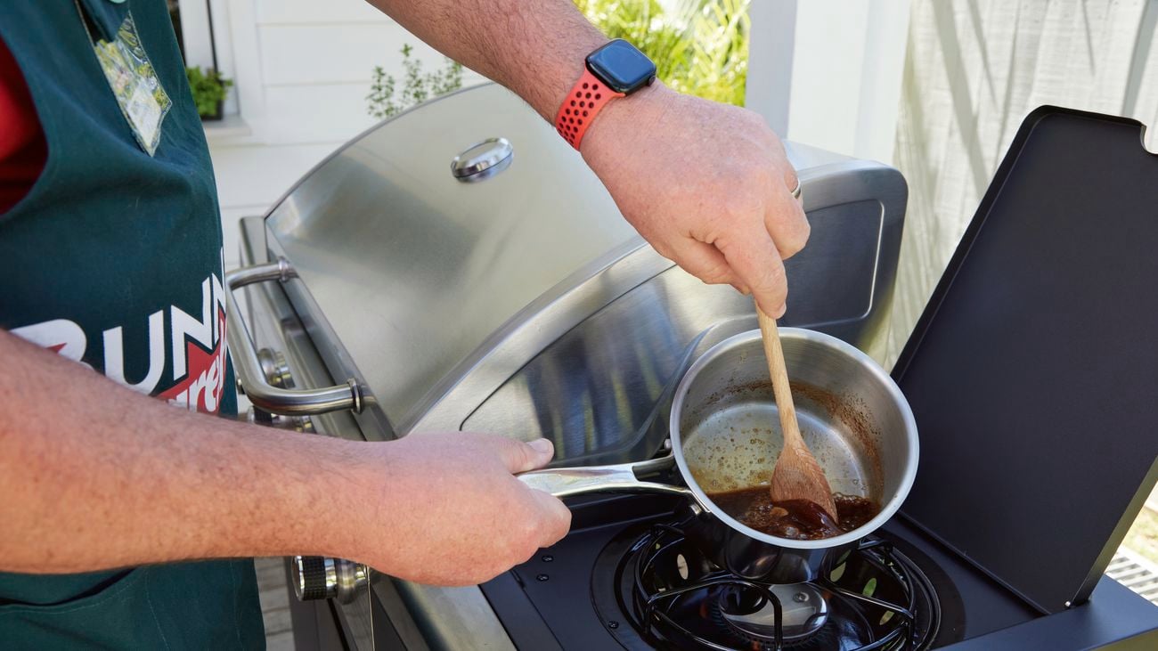 A Bunnings employee uses a wooden spoon to stir glaze in saucepan.
