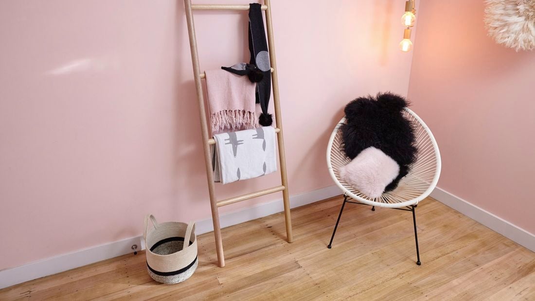 Room with pink wall, wooden ladder, basket and chair.