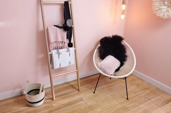 Room with pink wall, wooden ladder, basket and chair.