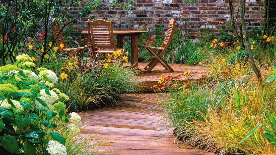 Wooden path with a table and chairs within a garden setting and flowering daffodils.