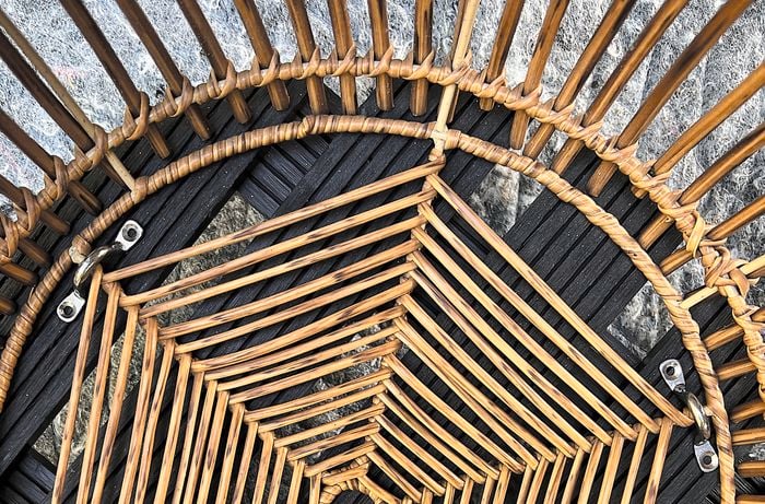 A rattan woven basket attached to a pot trolley with wire eye straps