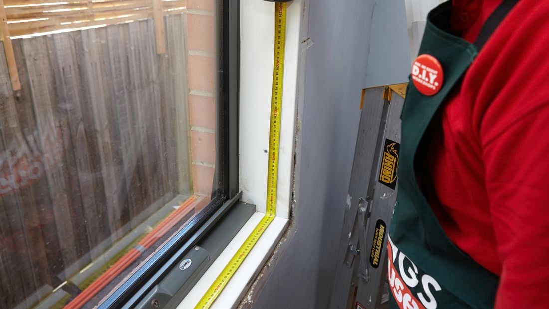 A person measuring the base of a window opening in a room