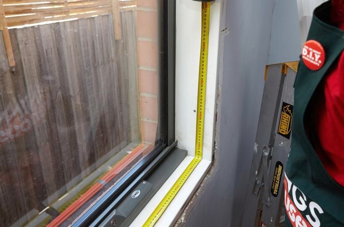 A person measuring the base of a window opening in a room