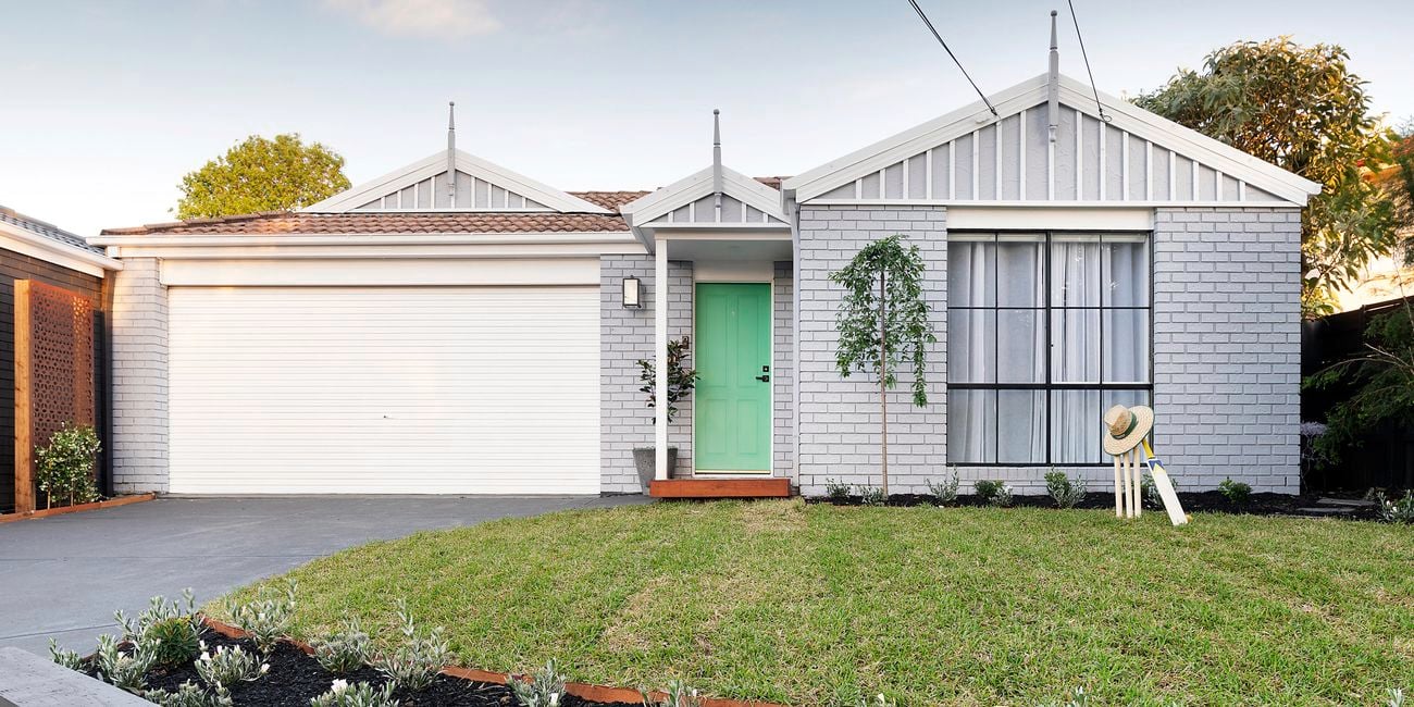 Front of brick house painted grey, with green lawn and neat garden.
