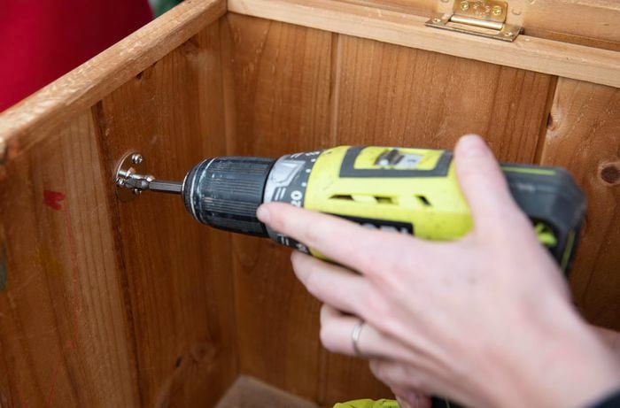 Person attaching bracket to the inside of a wooden chest