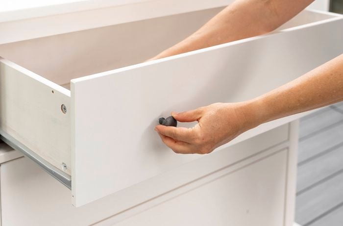 Hand pulling open a white cabinet drawer using a small round knob.