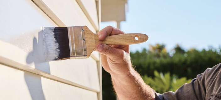 man painting the exterior of a timber house