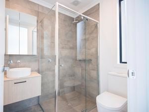 A fitted glass shower screen in a stone themed bathroom setting with nearby sink and toilet