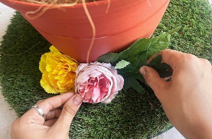 Hands attach artificial flowers on the artificial turf glued to the Easter hat.