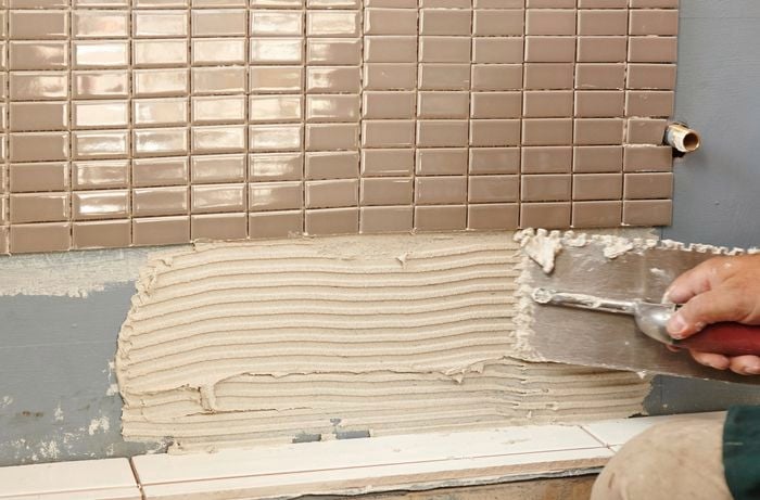 Tile adhesive being applied to a wall with a notched trowel by a Bunnings team member