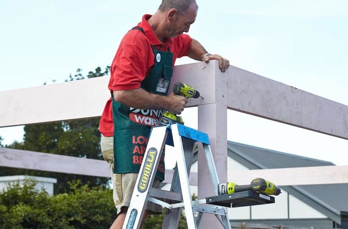 Bunnings team member standing on a ladder drilling a beam into a standing post