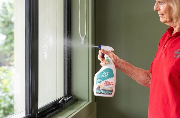 A Bunnings team member is spraying a "Window Wonder" glass cleaner on an interior window.