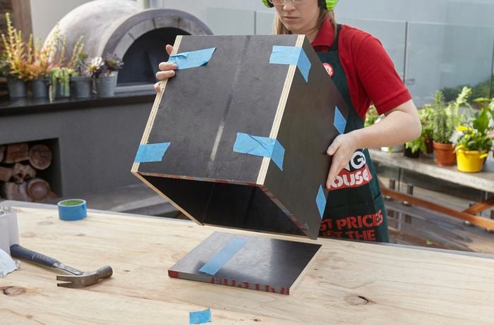 The frame of a wooden storage box being placed down over the base of the box for nailing into place