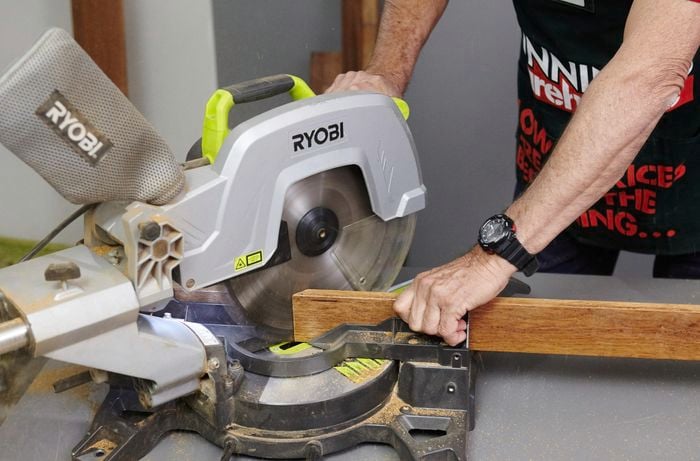 Person using circular saw to cut piece of timber into two pieces.