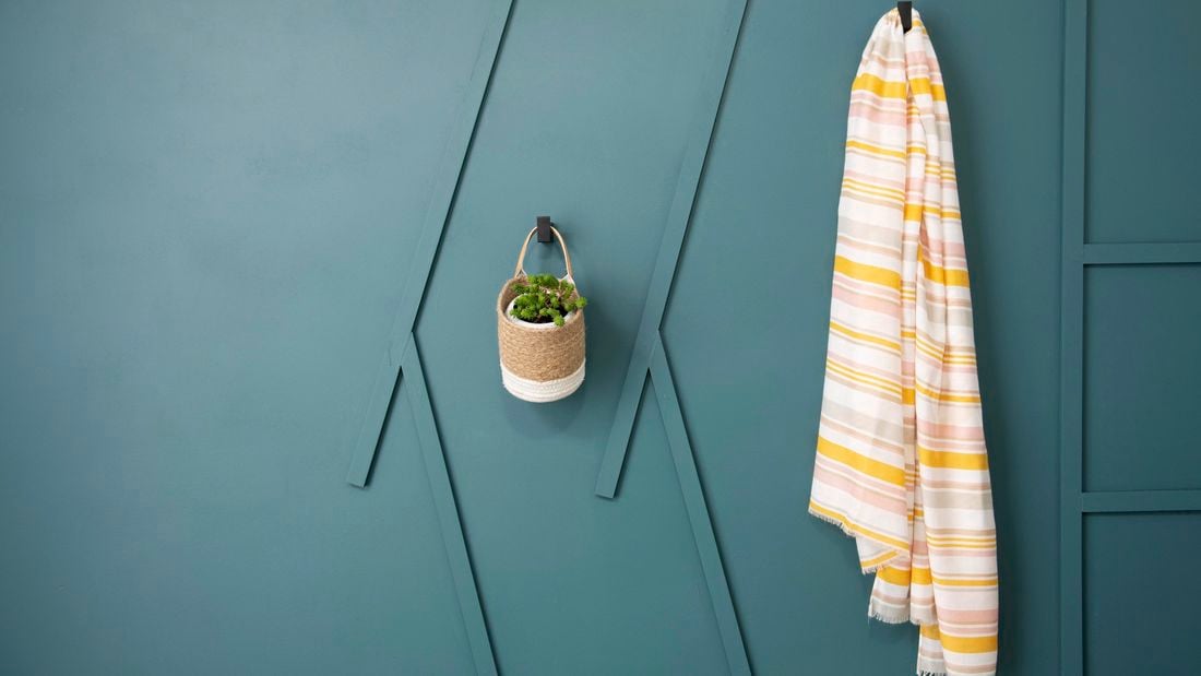 Small pot plant basket and towel hanging off green wall.