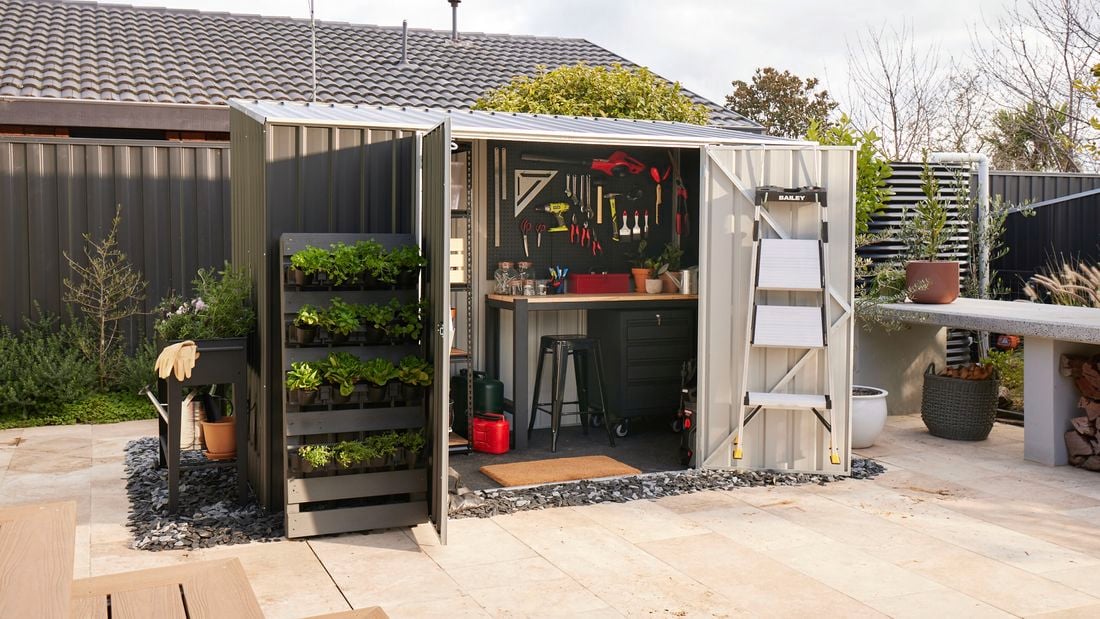 Dark shed in garden with doors open to show interior pegboard with tools attached and wooden desk