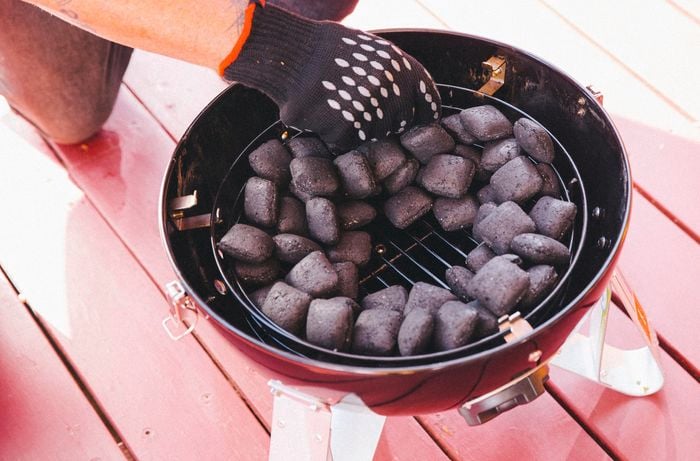 Person arranging charcoal in a smoker basket