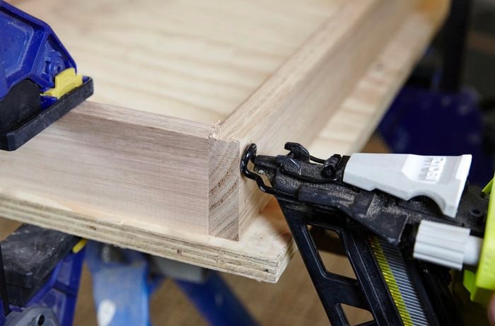 Pieces of timber clamped together while person nails together