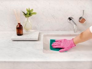 Hand in pink glove uses green cloth to wipe basin.