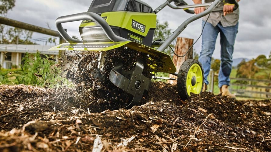 A person operating a front tine tiller to till the soil in a garden bed.