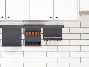 A wall with white tiles on it, white cupboards attached to it and black wall-mounted kitchen storage racks.