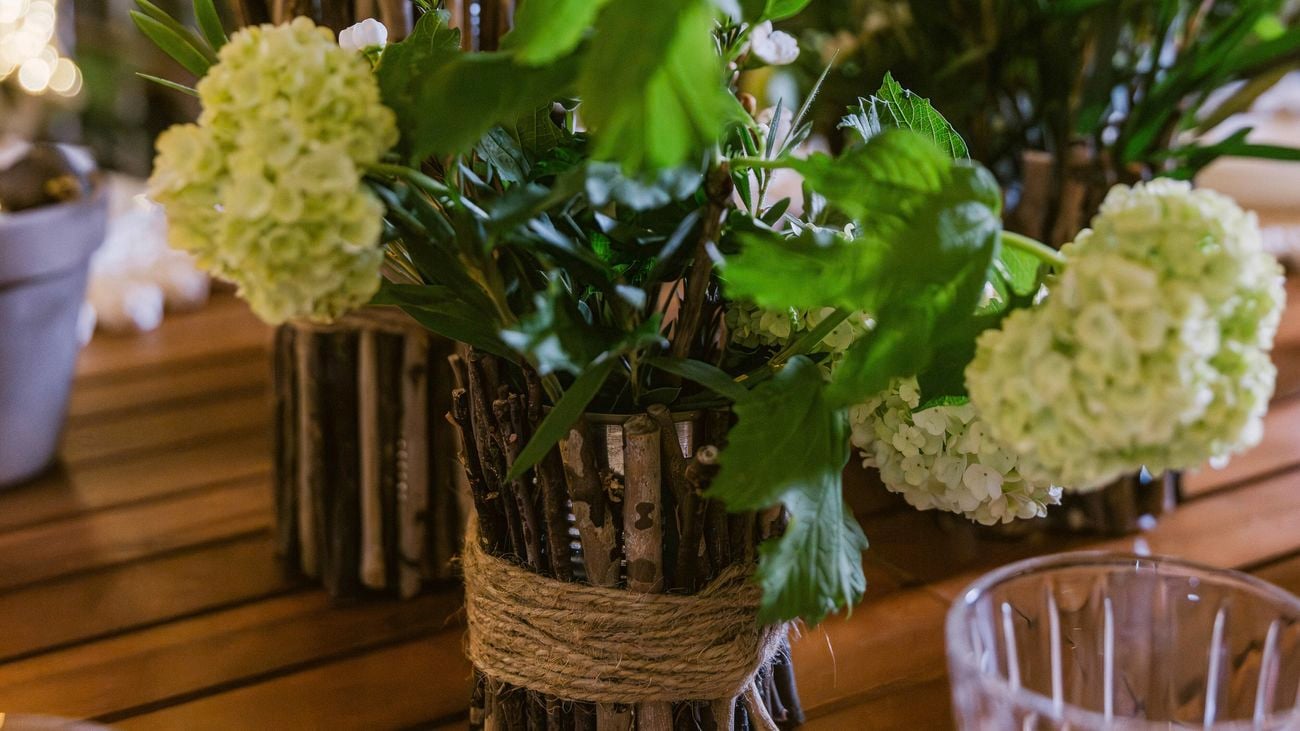 Rustic floral arrangement in a twig vase on a wooden dining table with glassware.