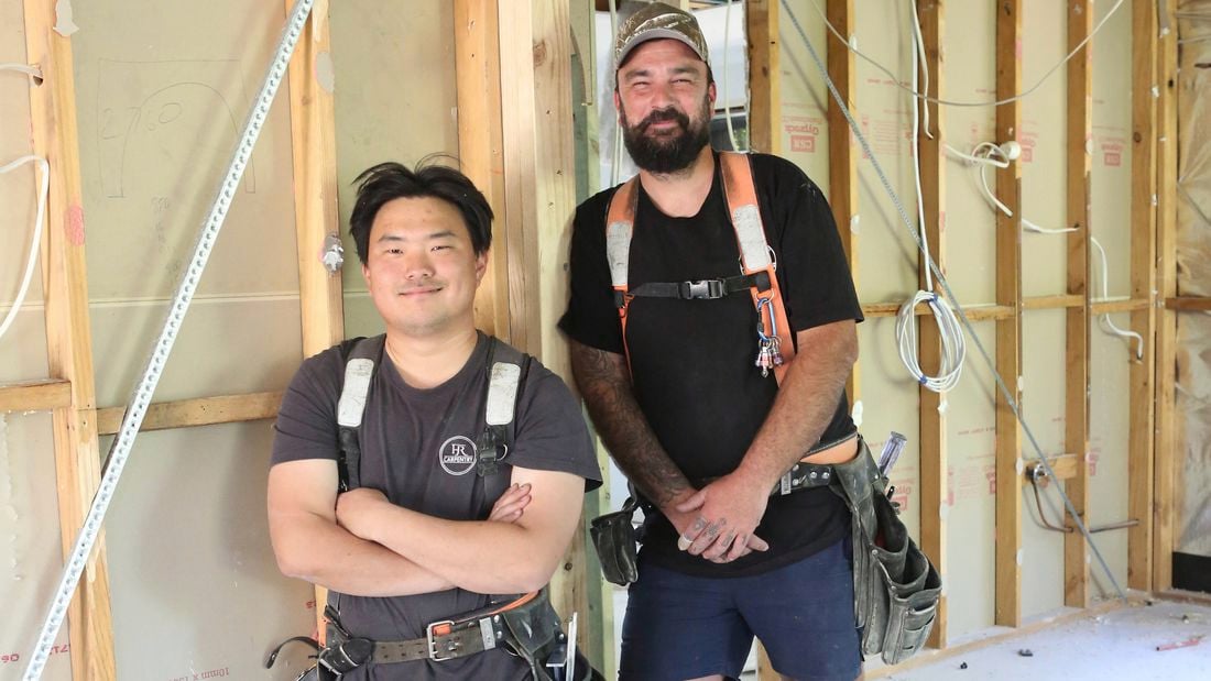 : Two tradies on a job site, one with arms crossed the other with hands in front, both smiling.