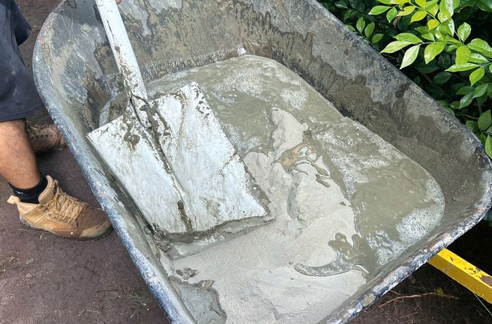 A wheelbarrow filled with mortar being mixed by a square-mouth shovel
