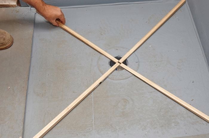 A person placing four wedge-shaped lengths of timber in an X across a shower base