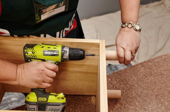The top bench surface of a wooden storage bench being screwed down by a Bunnings team member