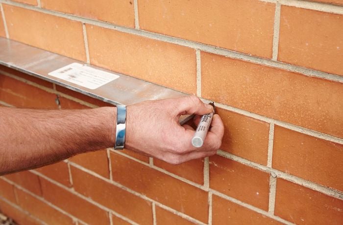 A person marking a brick wall using a metal lintel and marker pen