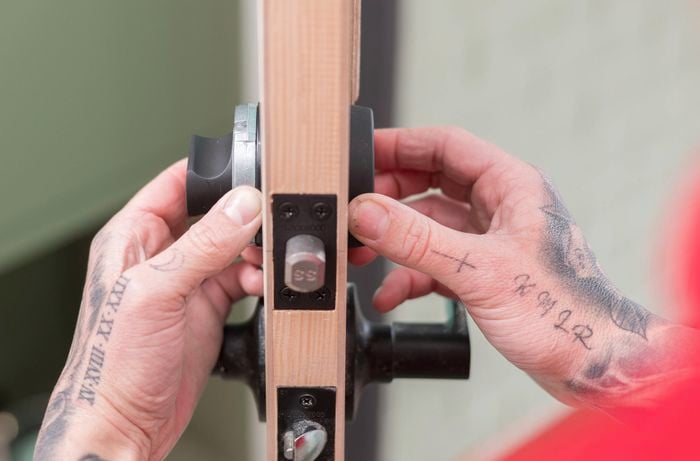 A person in red T shirt is positioning a lock cylinder on the edge of the door.