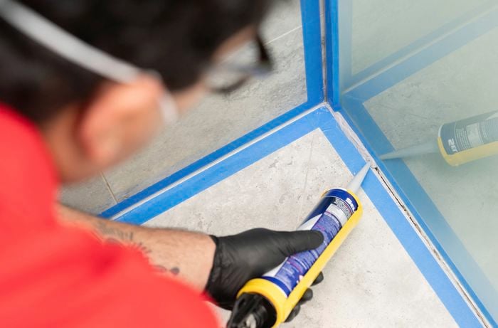  A person is ​applying a bead​ of silicone sealant along a taped joint using a caulking gun.​] 