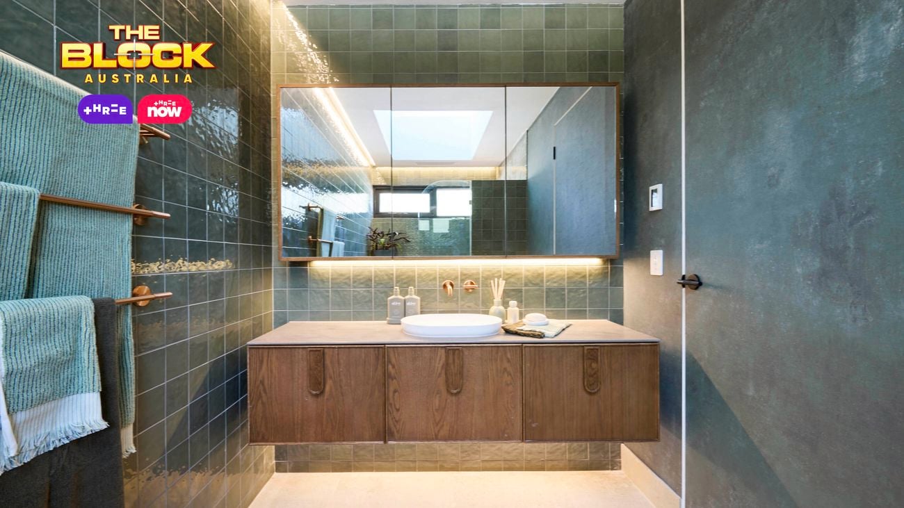 Modern bathroom with green tiles, wooden vanity, and backlit mirror.