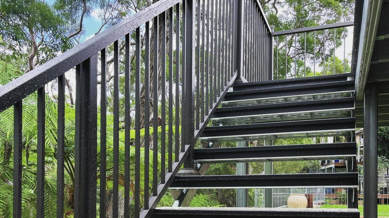 A set of outdoor stairs with black metal railings leading down into a garden area