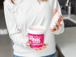 A lady holding a tub of The Pink Stuff with the lid off of the tub.