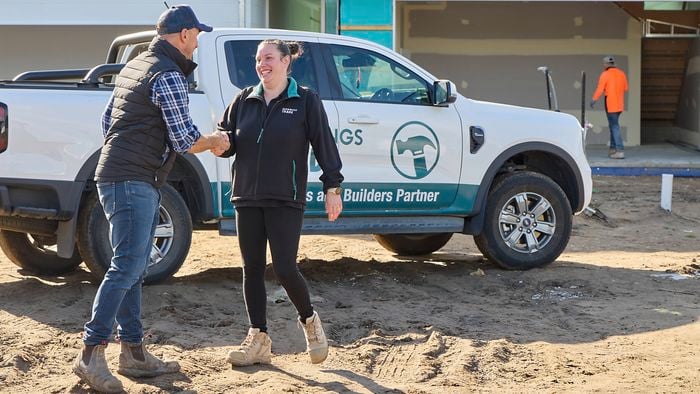 Two people shaking hands on a construction site beside a Bunnings-branded ute, with a building under construction in the background.