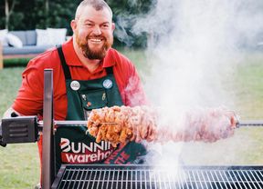 Man standing next to a spit roaster with meat on a rotisserie
