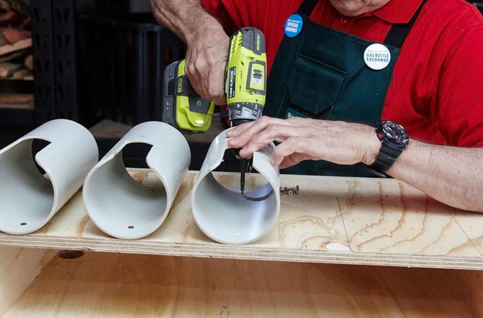 A person attaching a length of PVC pipe to a timber shelving unit using a cordless drill