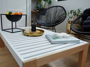 DIY slatted coffee table with assorted things on top and black chairs in background.