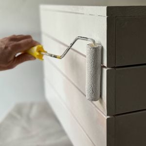 A hand uses a roller to paint the planter bench