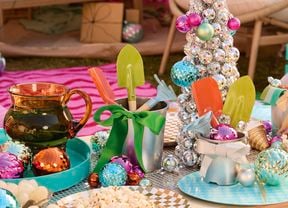 A table decorated with a silver bauble tree, colourful ornaments, small garden tools in silver buckets and plates of popcorn.