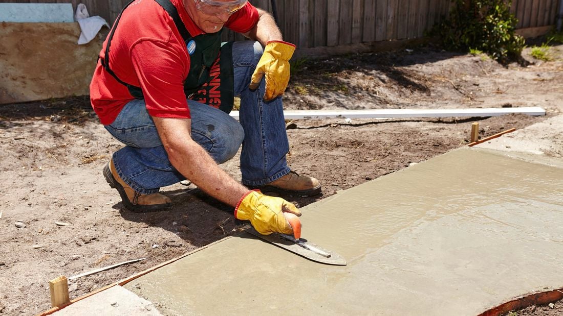 Bunnings team member using a trowel to smooth the wet concrete of an outdoor pathway